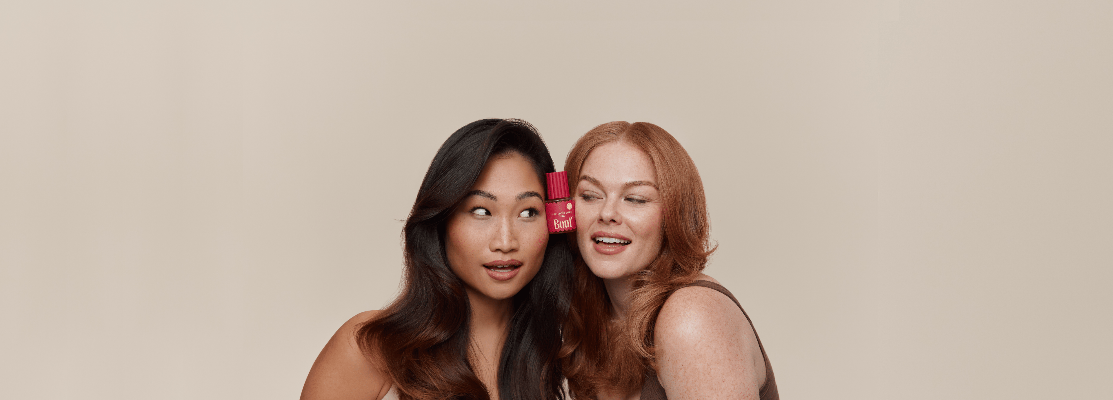 Two women with different hair colours holding the Flouf Factor Growth Tonic against a beige background